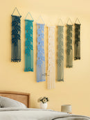 Five macrame wall hangings in various colors on a yellow wall above a bed.