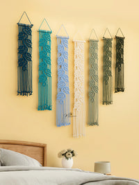 Five macrame wall hangings in various colors on a yellow wall above a bed.