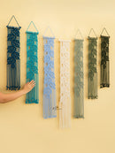 Set of six macrame wall hangings in various colors on a beige wall.