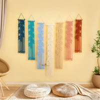 Set of colorful macrame wall hangings on a yellow wall with a wicker chair and plant in the foreground.