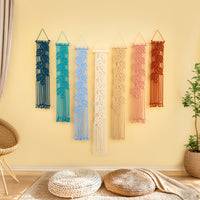 Colorful macrame wall hangings on a yellow wall with a woven chair and plant in the foreground.