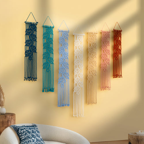Set of six colorful macrame wall hangings on a yellow wall.