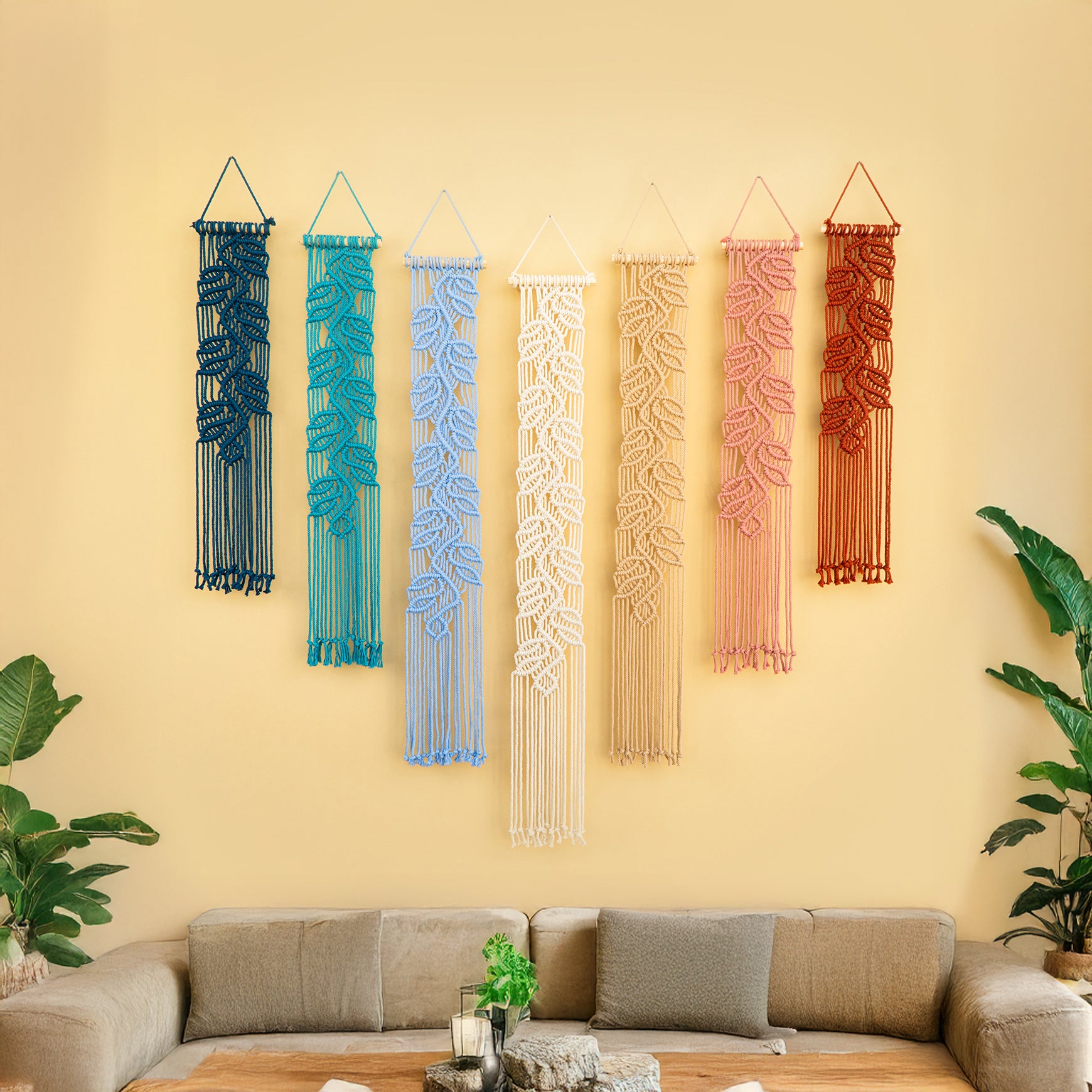 Colorful macrame wall hangings on a yellow wall above a sofa.