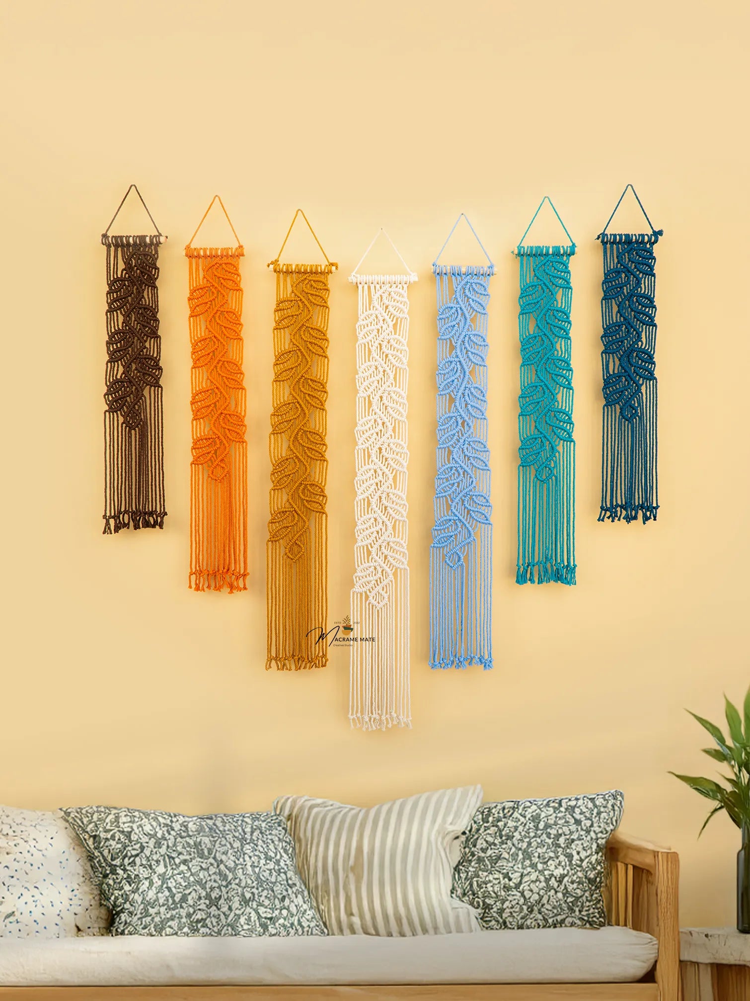 Set of colorful wall hangings on a beige wall above a sofa with decorative pillows.