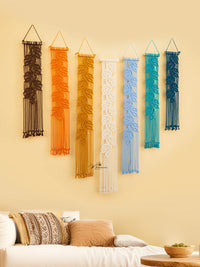 Set of six colorful wall hangings on a beige wall above a sofa.