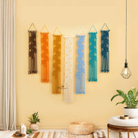 Decorative wall hangings in various colors on a yellow wall with a plant and table in the foreground.