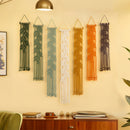 Long vertical olive macrame tapestry hung alongside warm earth-tone decor above green low seating