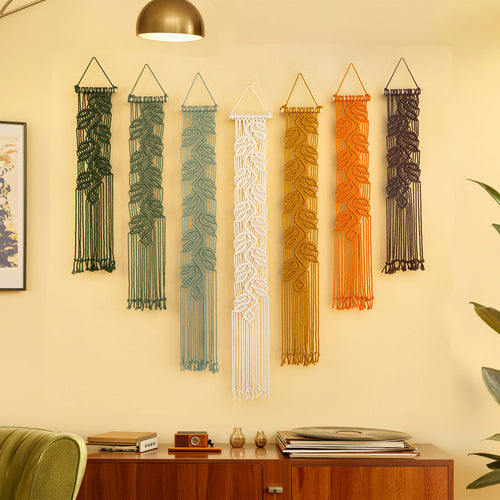 Long vertical olive macrame tapestry hung alongside warm earth-tone decor above green low seating