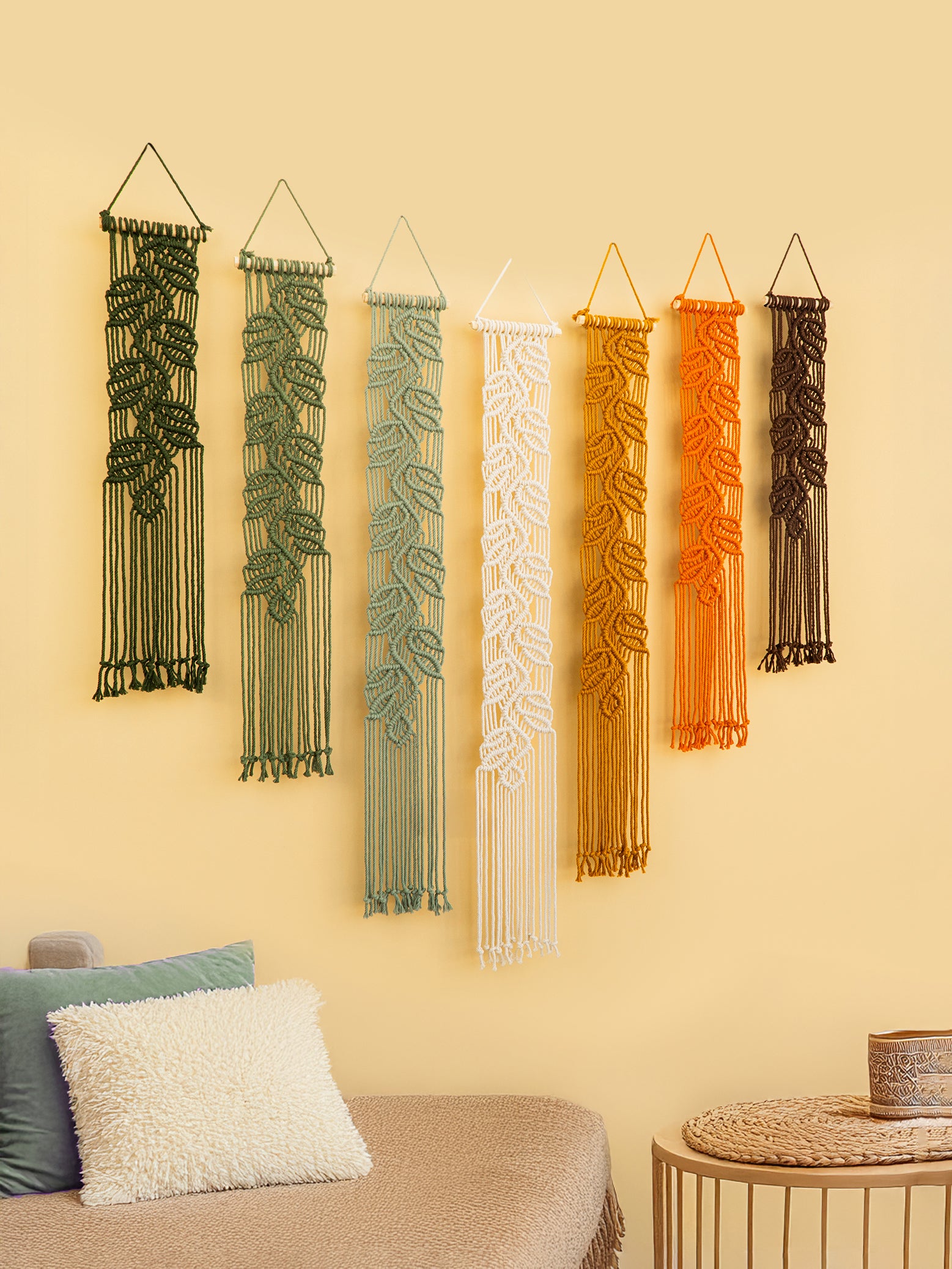 Set of five macrame wall hangings in various colors on a beige wall.