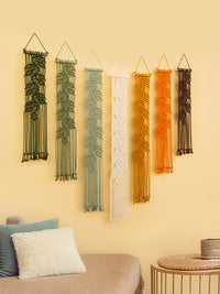 Set of five macrame wall hangings in various colors on a beige wall.