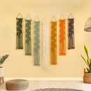 Set of six macrame wall hangings in various colors on a beige wall.