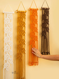 Four macrame wall hangings in white, beige, orange, and black on a yellow background.