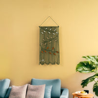 Decorative wall hanging with green leaves on a yellow wall above a blue sofa.