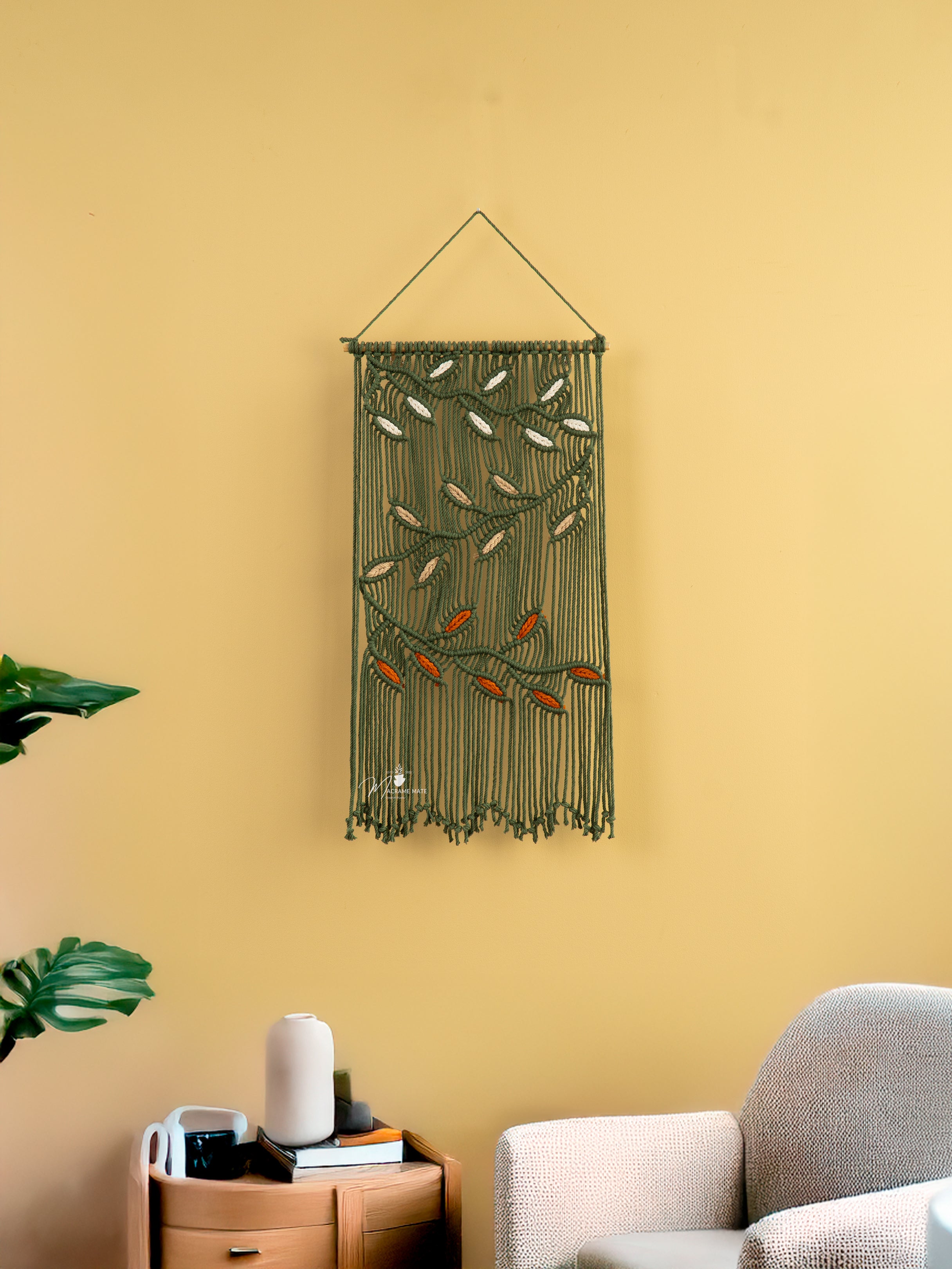 Decorative wall hanging with fringe on a yellow wall above a sofa.