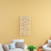 Macrame wall hanging with leaf patterns on a yellow wall above a white sofa.