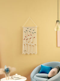 Decorative wall hanging with leaf patterns on a yellow wall above a sofa.