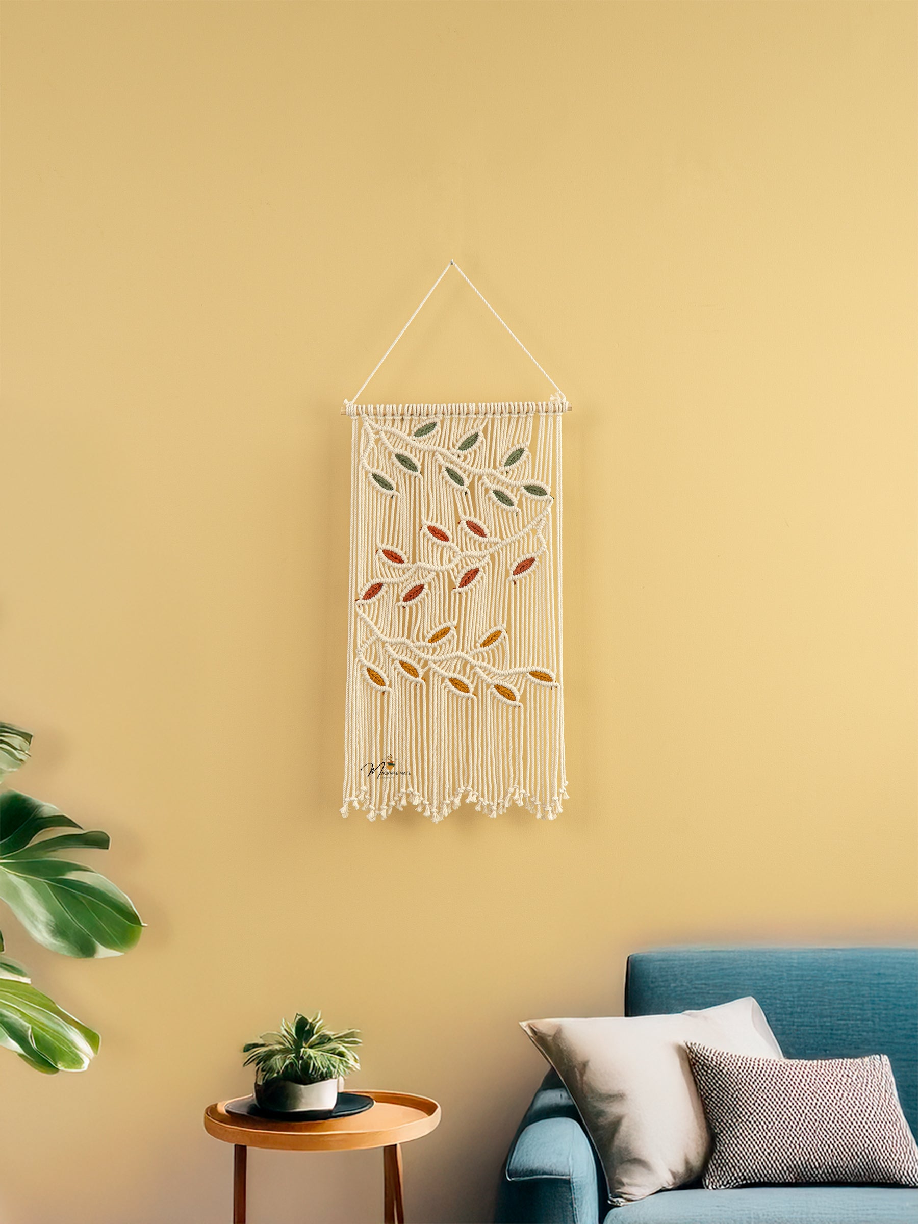 Decorative wall hanging with leaf patterns on a yellow wall above a blue sofa.