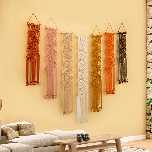 Set of six macrame wall hangings in various colors on a beige wall.