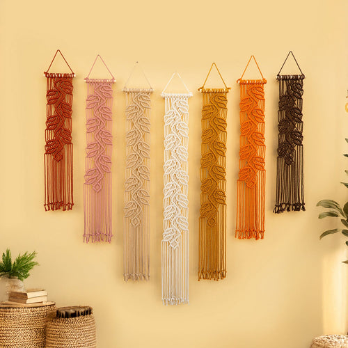 Set of five macrame wall hangings in various colors on a beige wall.