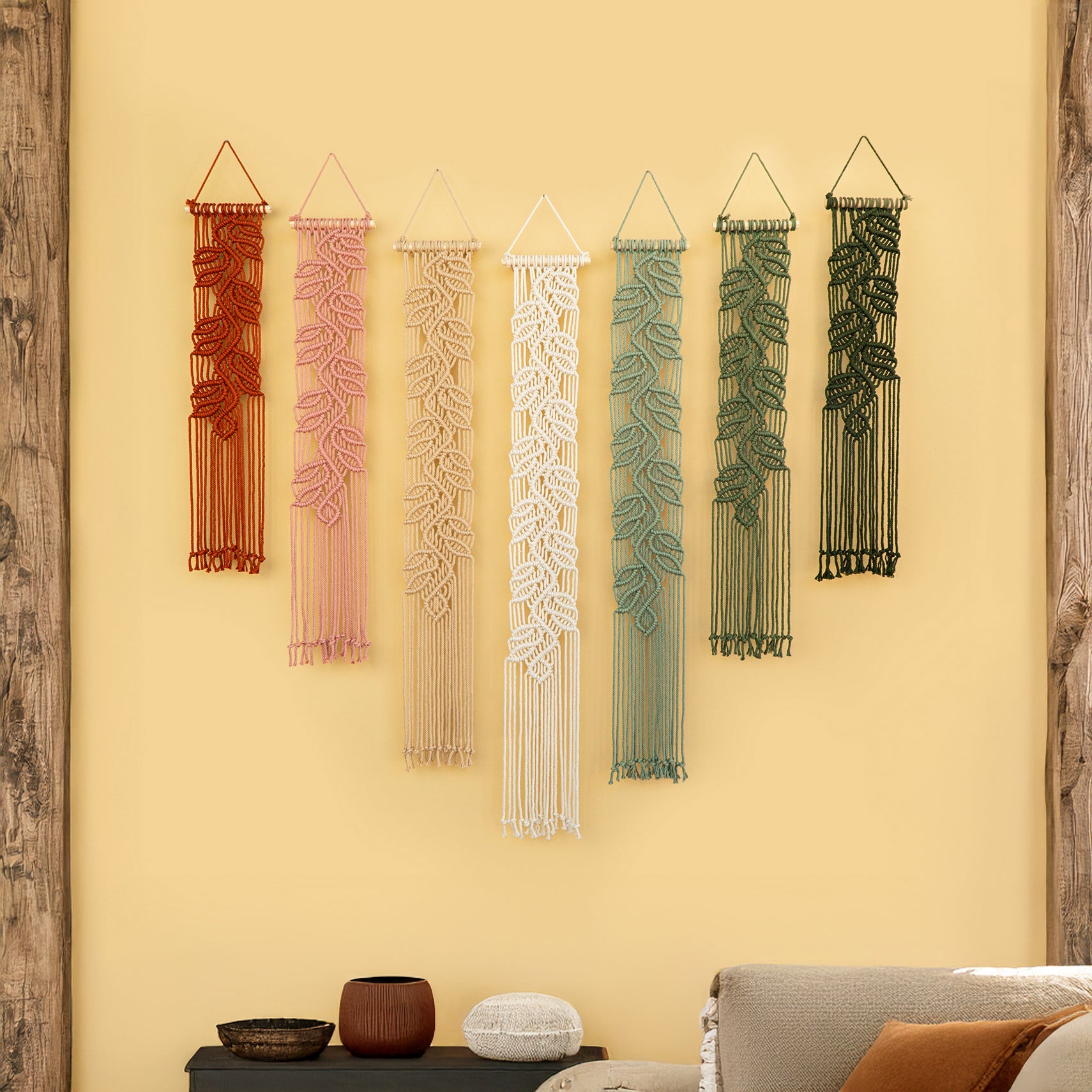 Set of six string art pieces in various colors hanging on a yellow wall.