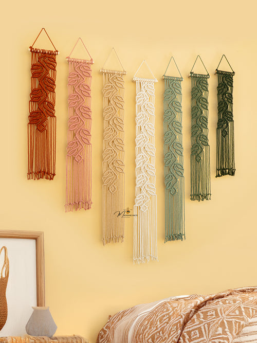 Set of five macrame wall hangings in various colors on a yellow wall.