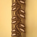 A close-up of a decorative braided cord trim or macrame pattern in dark brown and cream, shown vertically against a solid warm beige background.