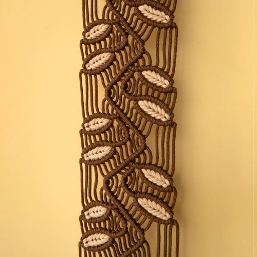 A close-up of a decorative braided cord trim or macrame pattern in dark brown and cream, shown vertically against a solid warm beige background.