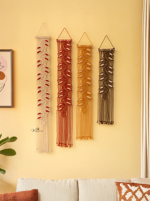Four string wall art pieces in different colors hanging on a yellow wall.