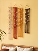 Four macrame wall hangings in different colors on a beige wall.