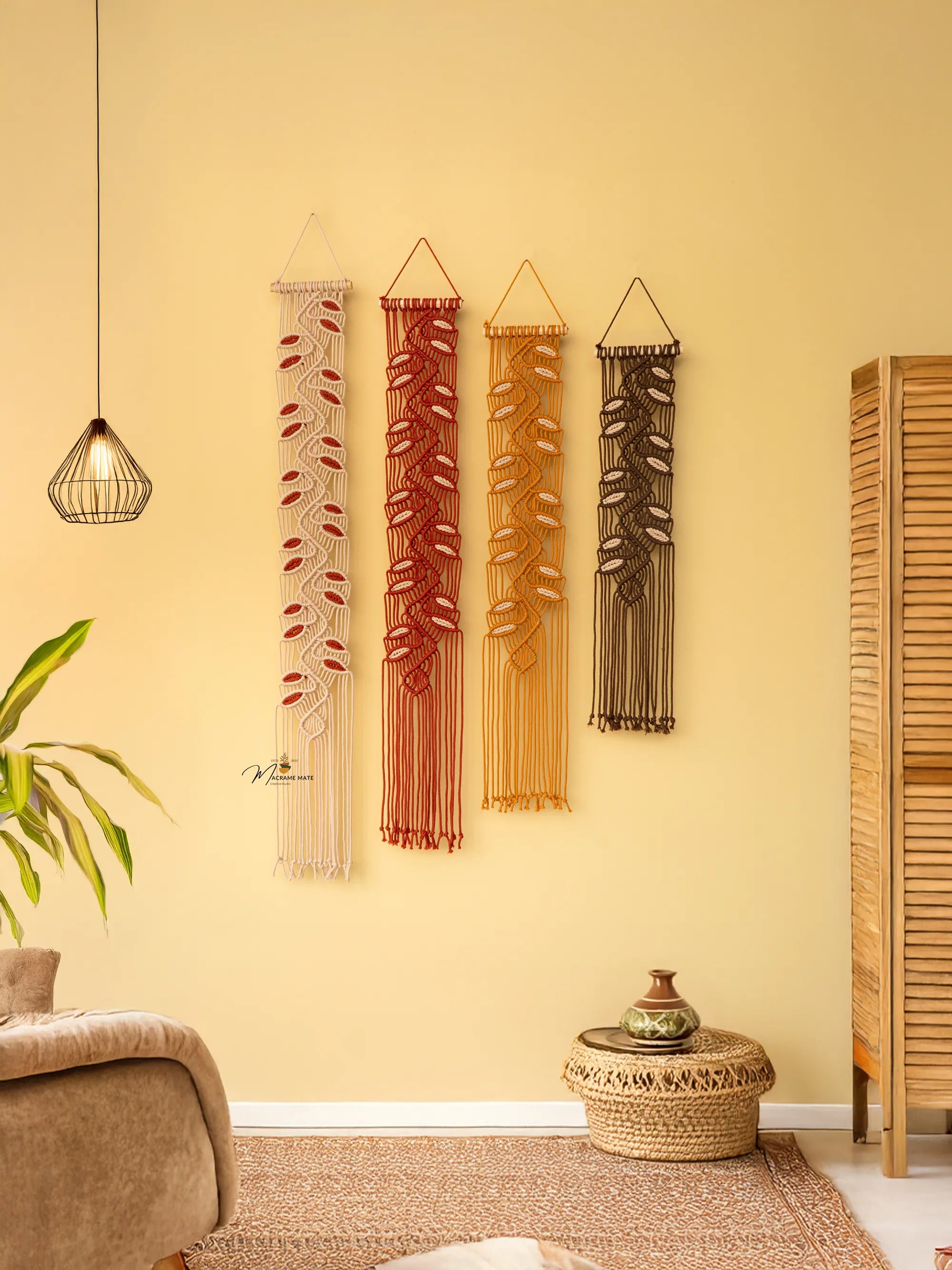 Four woven wall hangings in various patterns and colors on a yellow wall, with a plant and wooden cabinet in the foreground.