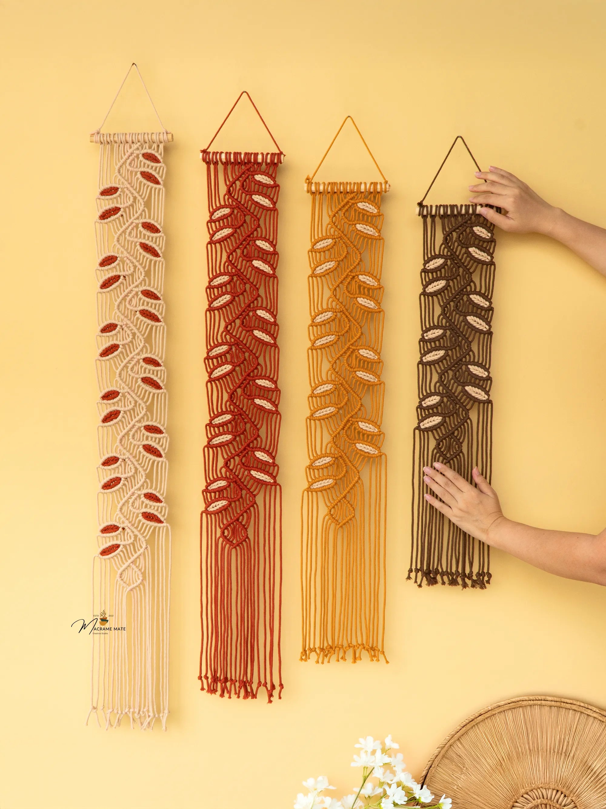 Four macrame wall hangings of different colors on a yellow background