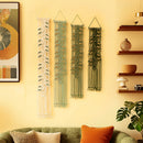 Three bohemian-style macrame wall hangings with leaf patterns in cream, sage green, and dark green, displayed on a warm yellow wall above a green sofa in a styled living room.