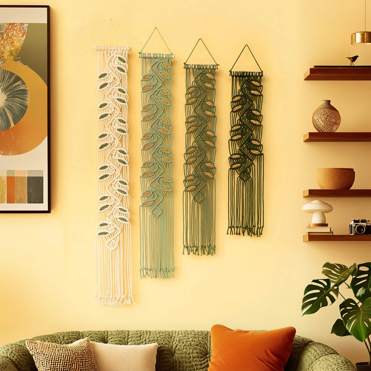 Three bohemian-style macrame wall hangings with leaf patterns in cream, sage green, and dark green, displayed on a warm yellow wall above a green sofa in a styled living room.