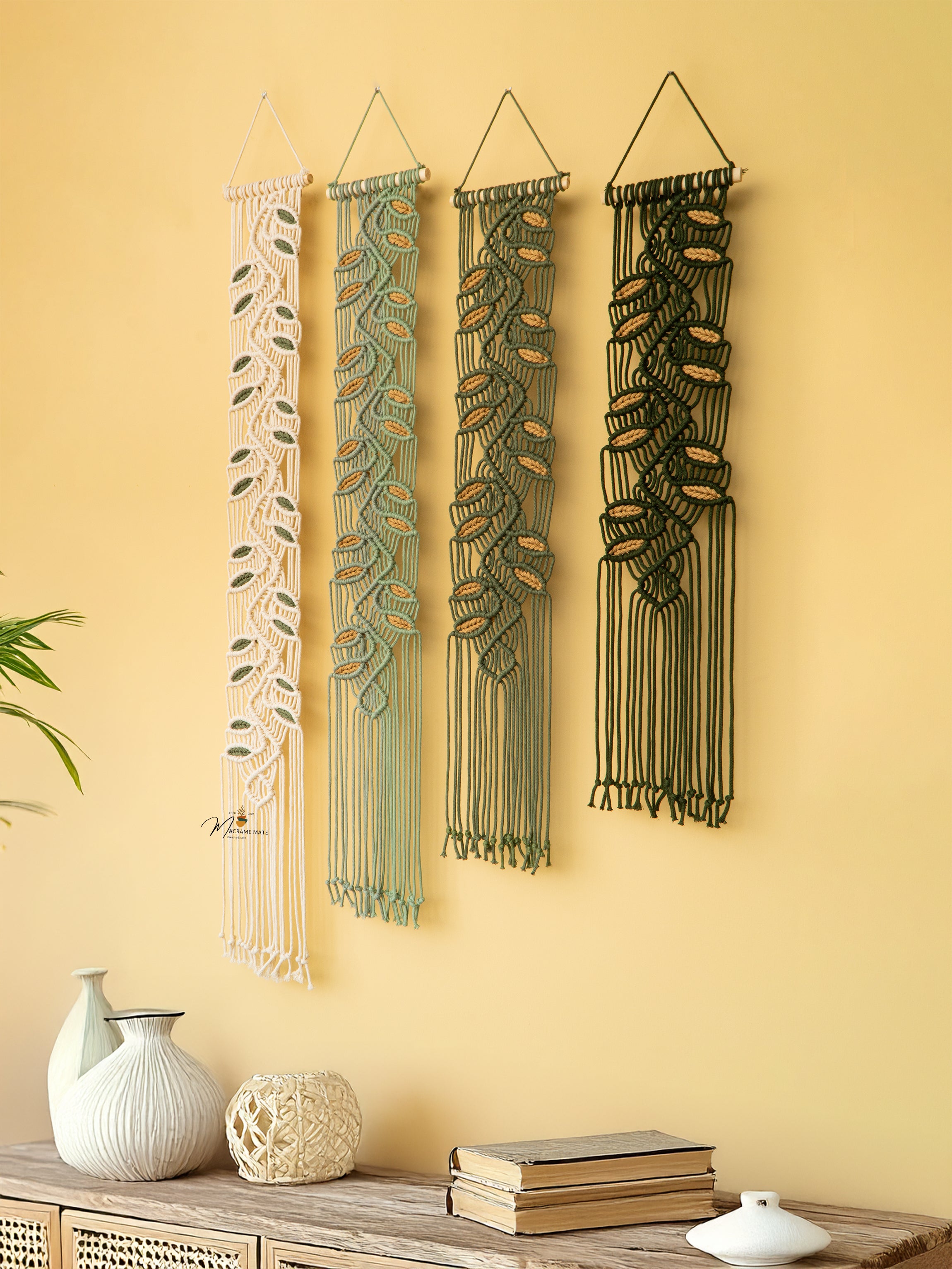Four macrame wall hangings on a yellow wall with decorative items below.