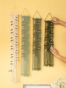 Four woven wall hangings on a yellow wall with a hand reaching for one of them.