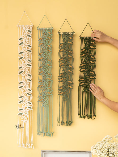 Four woven wall hangings on a yellow wall with a hand reaching for one of them.