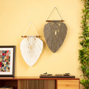Two bohemian macrame wall hangings, one white and one gray, hanging on a yellow wall above a wooden console table with a plant and framed art.